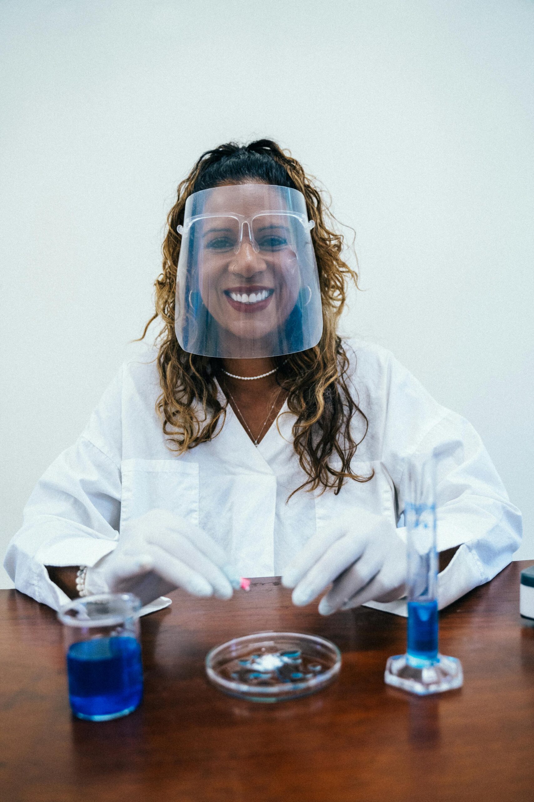 A smiling scientist in protective gear conducts experiments with lab glassware indoors.